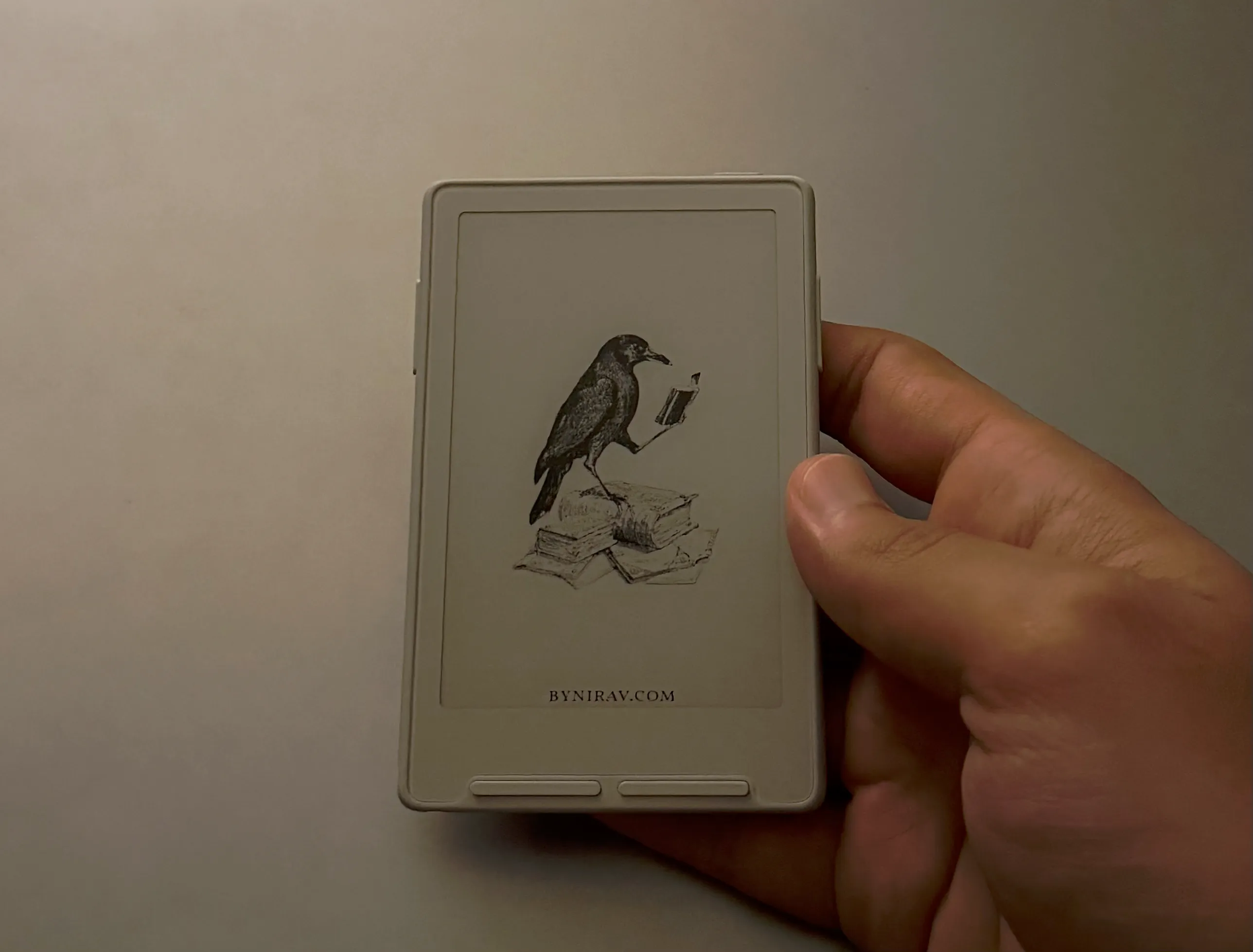 a XTeink device held in hand with crow screensaver with bynirav.com written
