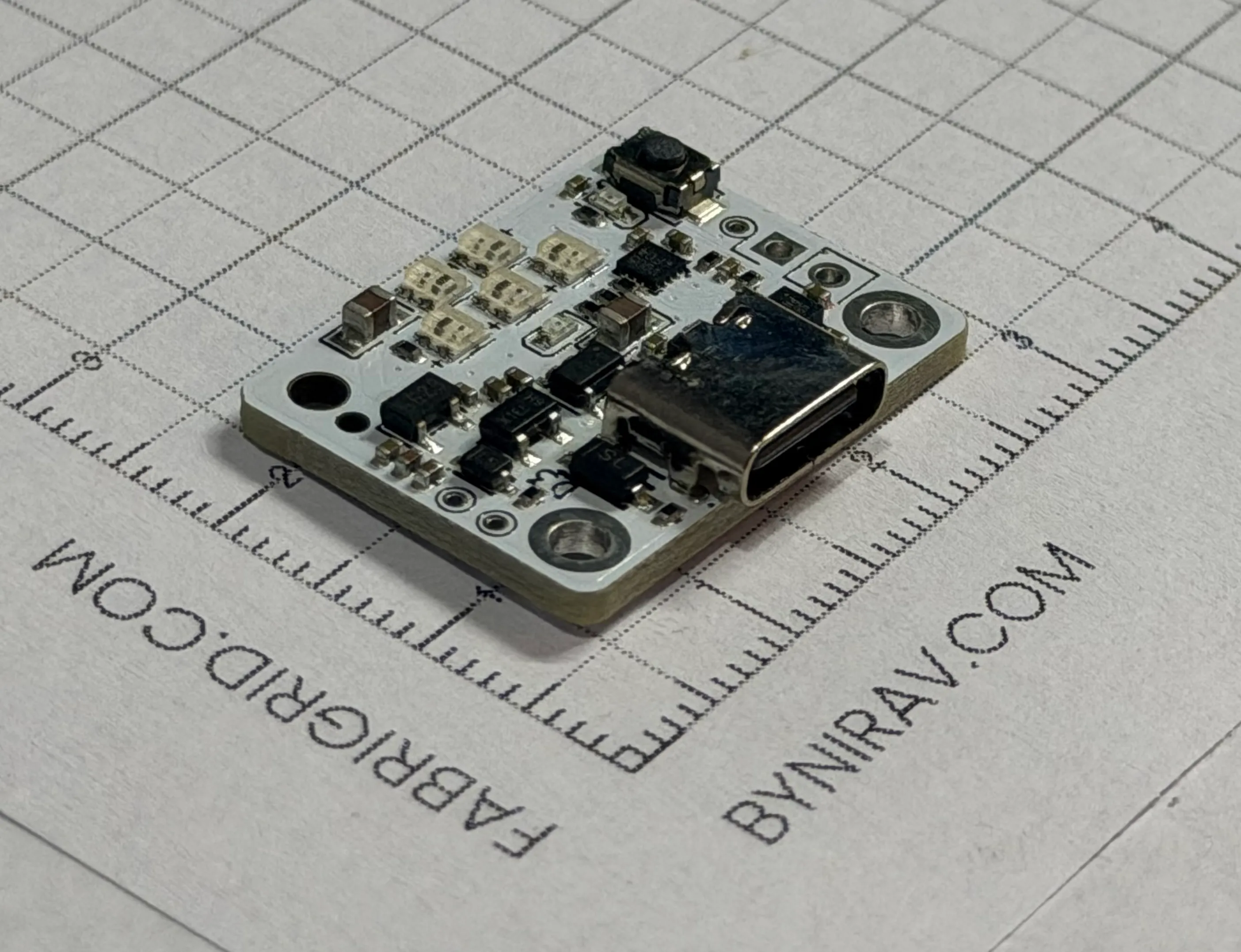 A small white circuit board on graph paper with five tiny LEDs, a USB-C port and a push button